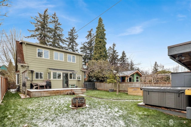 back of house featuring an outdoor fire pit, a hot tub, a deck, and a yard