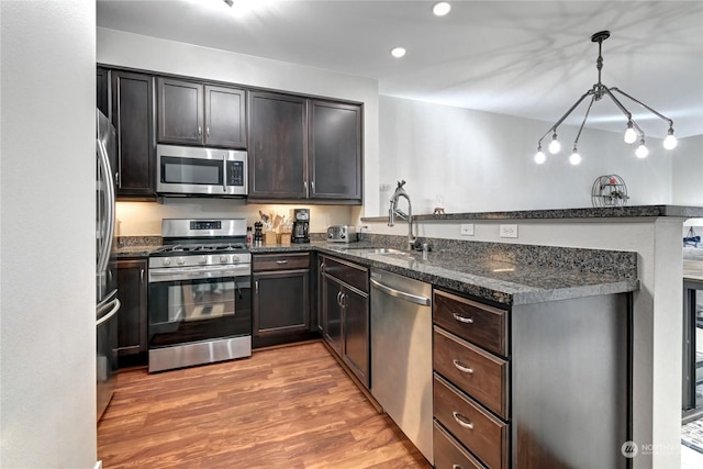 kitchen with sink, wood-type flooring, decorative light fixtures, dark stone countertops, and stainless steel appliances