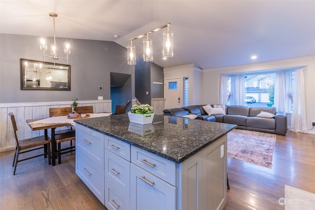 kitchen with lofted ceiling, dark stone countertops, hanging light fixtures, white cabinets, and a kitchen island