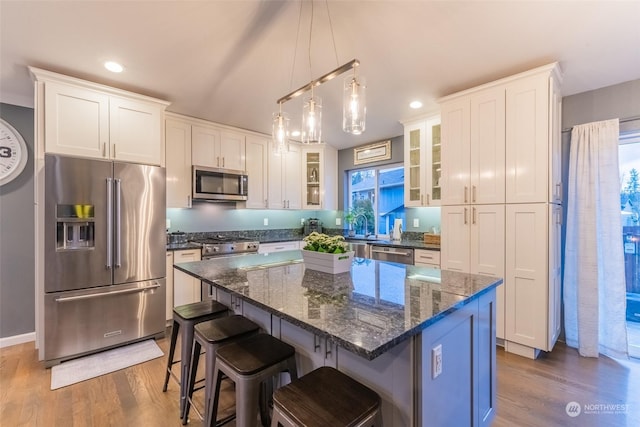 kitchen with a kitchen bar, high end appliances, white cabinetry, wood-type flooring, and a center island