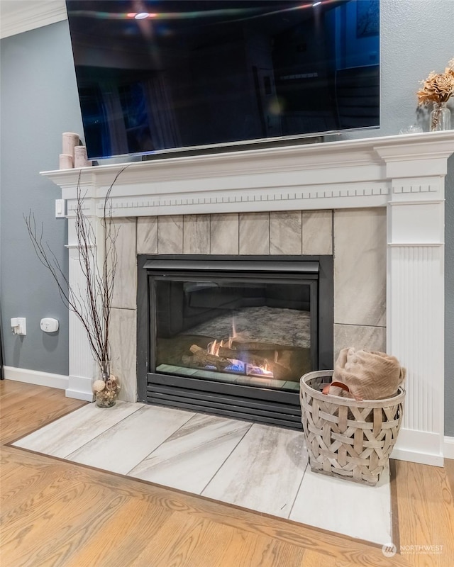 room details featuring a tile fireplace, ornamental molding, and hardwood / wood-style floors