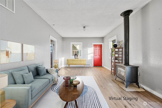 living room featuring baseboard heating, a wood stove, a textured ceiling, and light hardwood / wood-style flooring