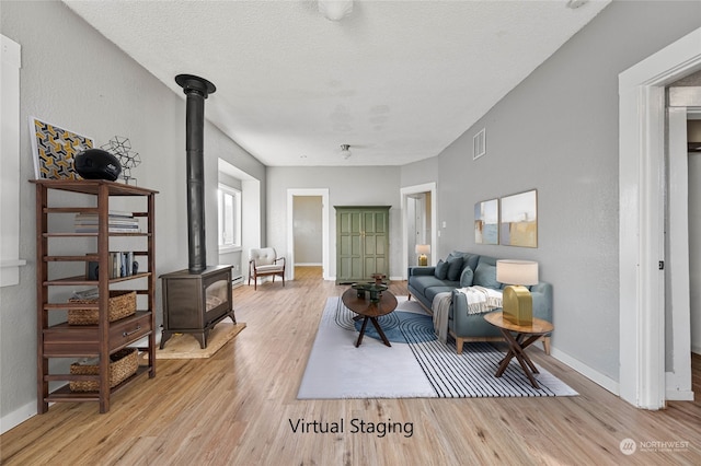 living room featuring light wood-type flooring, a textured ceiling, and a wood stove