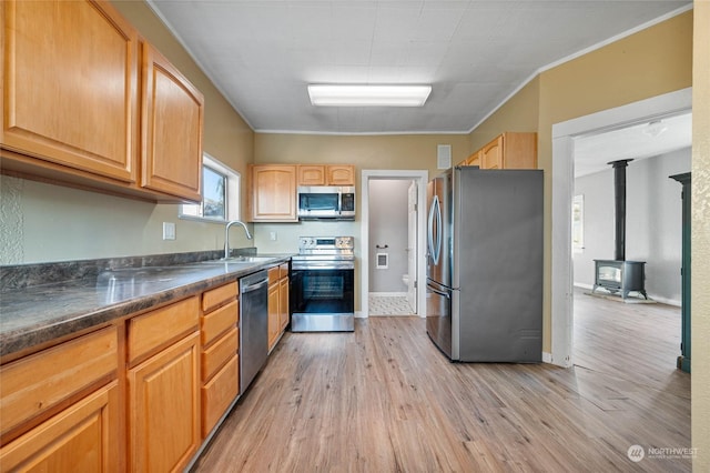 kitchen with sink, crown molding, stainless steel appliances, light hardwood / wood-style floors, and a wood stove