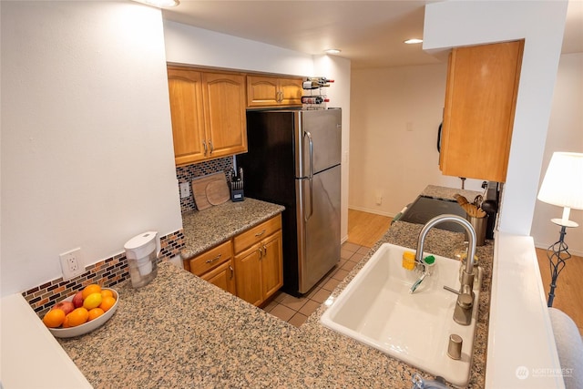 kitchen with sink, light stone counters, tasteful backsplash, light tile patterned floors, and stainless steel refrigerator