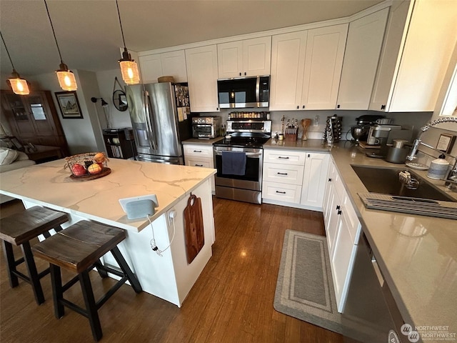 kitchen with appliances with stainless steel finishes, a breakfast bar area, white cabinets, hanging light fixtures, and light stone counters