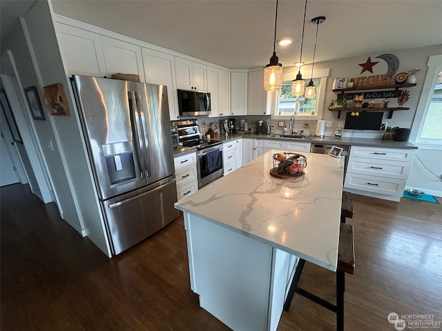 kitchen with white cabinetry, light stone counters, a kitchen island, pendant lighting, and stainless steel appliances