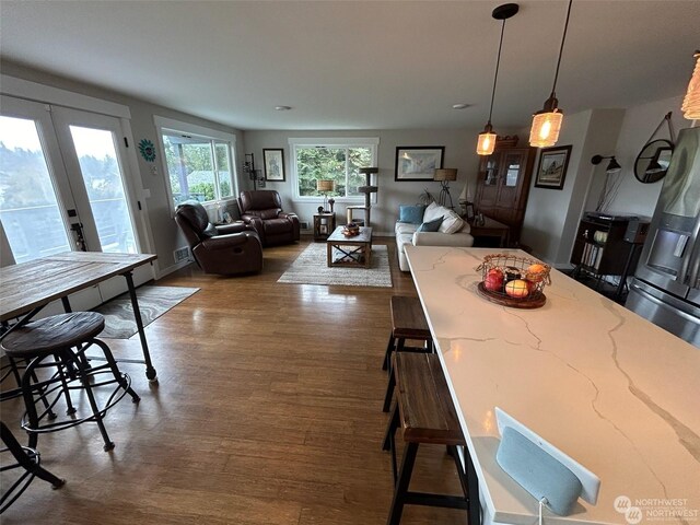 kitchen with a breakfast bar, pendant lighting, dark hardwood / wood-style floors, light stone countertops, and french doors