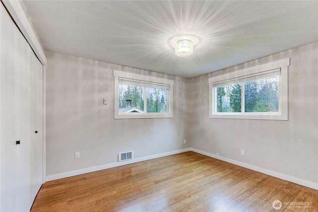 unfurnished bedroom featuring baseboards, a closet, visible vents, and wood finished floors