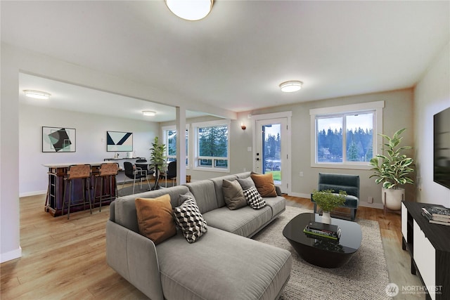 living area featuring a bar, light wood-style flooring, and baseboards