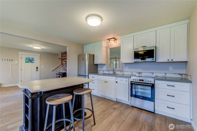 kitchen featuring a breakfast bar area, stainless steel appliances, a sink, white cabinets, and light wood-type flooring