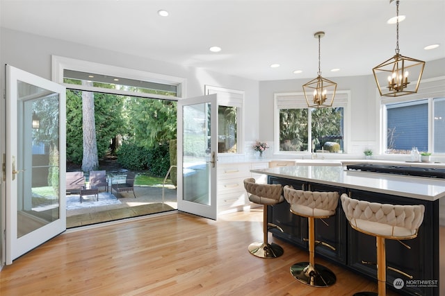 kitchen with pendant lighting, white cabinetry, a kitchen bar, light wood-type flooring, and french doors