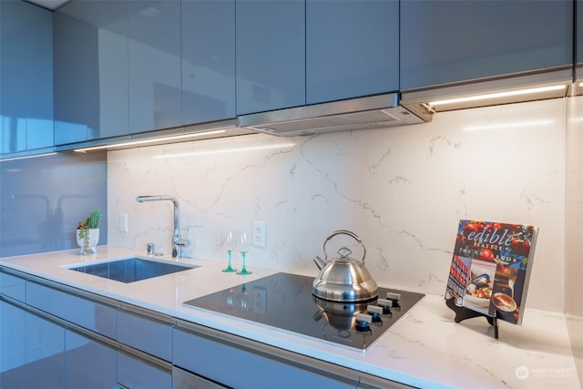 kitchen with blue cabinetry, black electric stovetop, sink, and backsplash