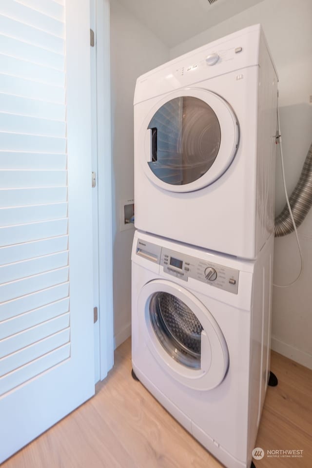 laundry area with light hardwood / wood-style flooring and stacked washing maching and dryer