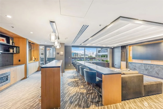 kitchen with stainless steel counters, a center island, a kitchen bar, decorative light fixtures, and light wood-type flooring