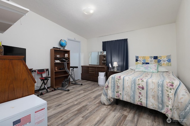 bedroom with light hardwood / wood-style floors, vaulted ceiling, and a textured ceiling