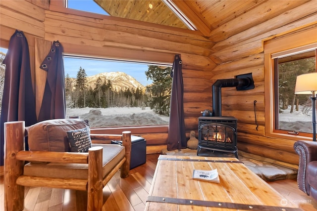 living area with wood-type flooring, a mountain view, a wood stove, and log walls