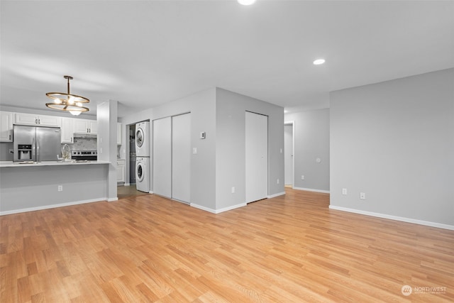 unfurnished living room featuring sink, a notable chandelier, light hardwood / wood-style floors, and stacked washer / dryer