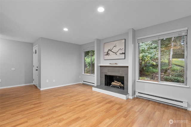 unfurnished living room with a tiled fireplace, a baseboard heating unit, and light hardwood / wood-style floors