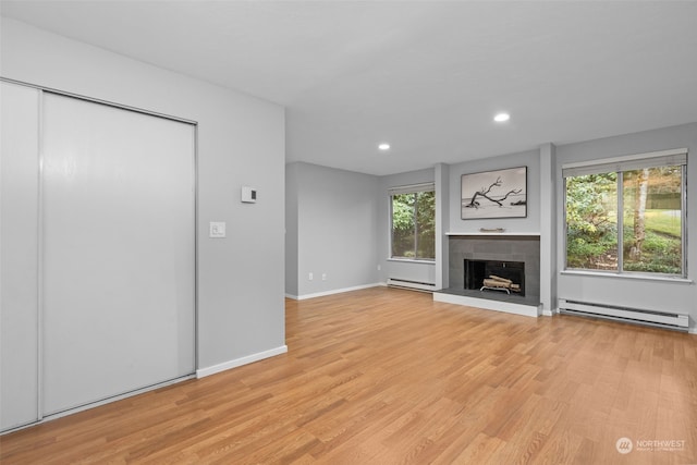 unfurnished living room featuring a baseboard heating unit, light hardwood / wood-style flooring, and a tile fireplace