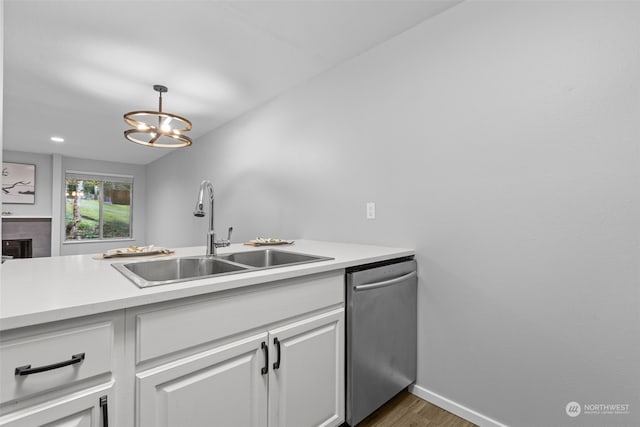 kitchen with a tile fireplace, decorative light fixtures, white cabinetry, sink, and stainless steel dishwasher