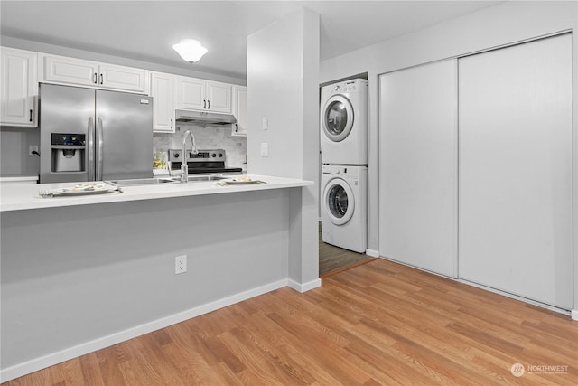 kitchen with appliances with stainless steel finishes, stacked washer and clothes dryer, white cabinets, and light hardwood / wood-style flooring