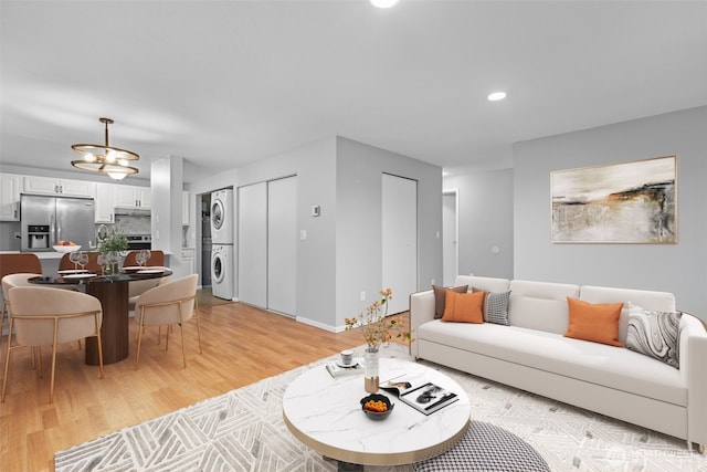 living area with baseboards, light wood-type flooring, stacked washer and dryer, recessed lighting, and a notable chandelier