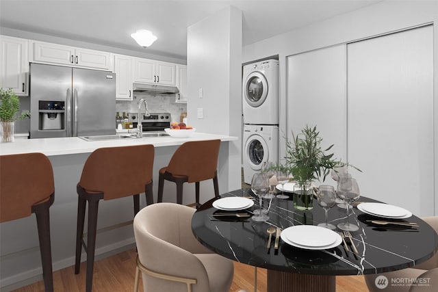 kitchen with a breakfast bar area, stainless steel fridge with ice dispenser, decorative backsplash, stacked washer and dryer, and under cabinet range hood