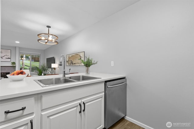 kitchen with light countertops, stainless steel dishwasher, wood finished floors, white cabinets, and a sink