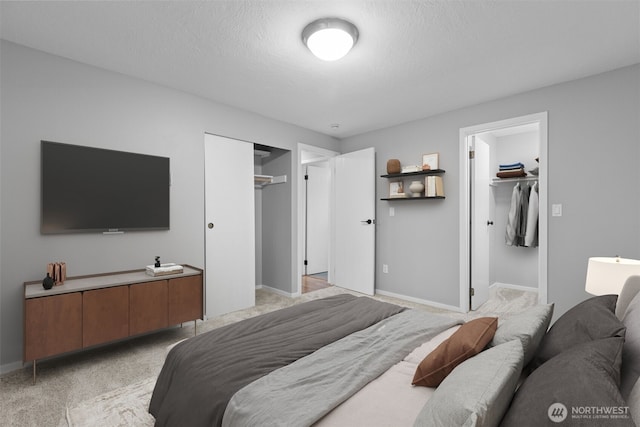 bedroom featuring a walk in closet, baseboards, light colored carpet, a closet, and a textured ceiling