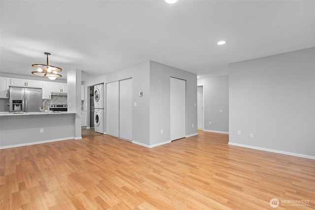 unfurnished living room with light wood-style flooring, a sink, stacked washer / dryer, baseboards, and a chandelier