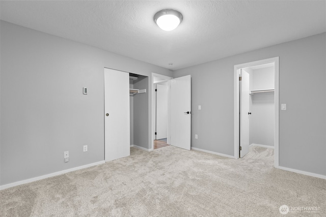 unfurnished bedroom with a walk in closet, a textured ceiling, a closet, carpet, and baseboards