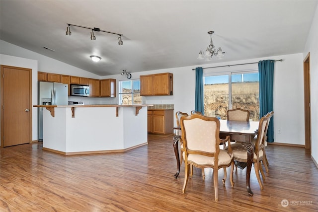 dining room with lofted ceiling, track lighting, a chandelier, and light wood-type flooring