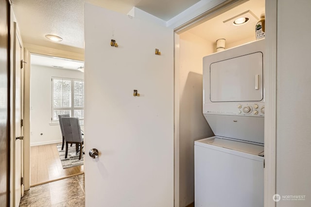 laundry room featuring stacked washer / drying machine, light hardwood / wood-style floors, and a textured ceiling