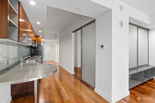 kitchen featuring stainless steel counters, sink, elevator, and light hardwood / wood-style flooring