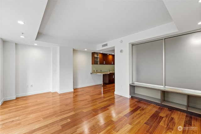 unfurnished living room featuring a tray ceiling and light hardwood / wood-style floors