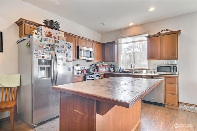 kitchen with sink, a center island, tile counters, stainless steel appliances, and light hardwood / wood-style floors