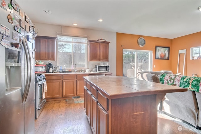 kitchen featuring sink, stainless steel appliances, tile counters, a kitchen island, and light wood-type flooring