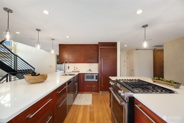 kitchen featuring pendant lighting, built in appliances, sink, and light wood-type flooring