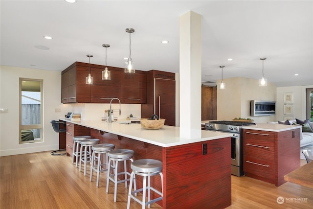 kitchen featuring gas range, pendant lighting, a kitchen breakfast bar, and light hardwood / wood-style floors