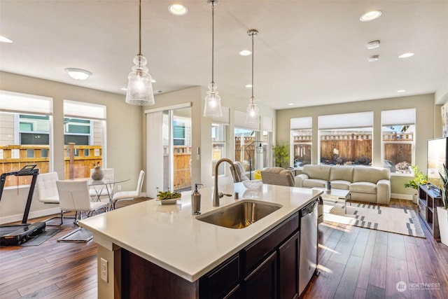 kitchen featuring dark wood-type flooring, sink, hanging light fixtures, dishwasher, and a kitchen island with sink