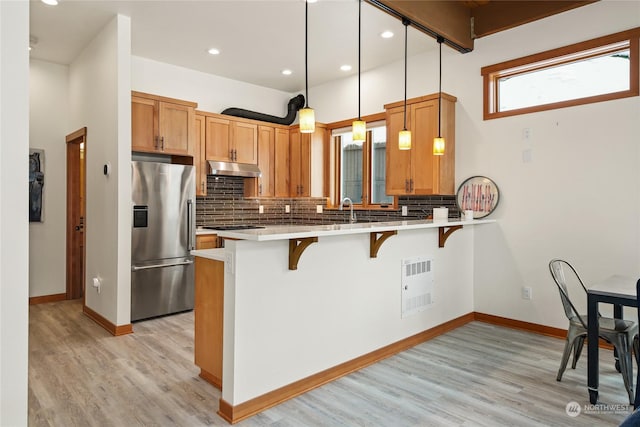 kitchen with a breakfast bar, decorative light fixtures, stainless steel fridge, kitchen peninsula, and tasteful backsplash