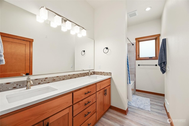 bathroom with hardwood / wood-style flooring, vanity, shower / bath combo, and backsplash