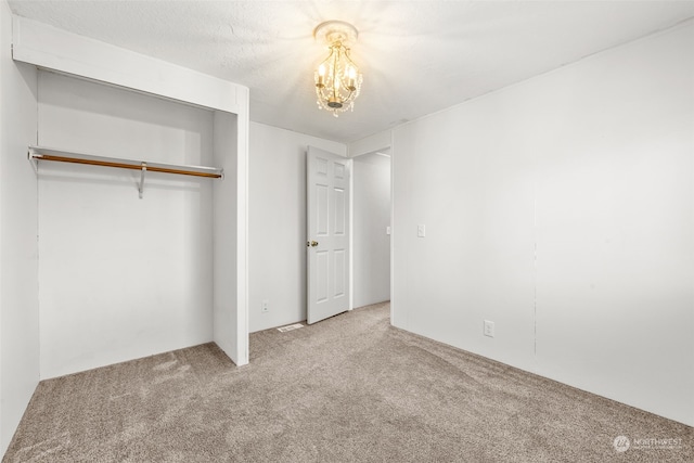 unfurnished bedroom with a notable chandelier, light colored carpet, a closet, and a textured ceiling