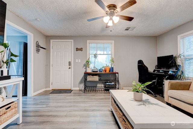 living room with a textured ceiling, light hardwood / wood-style floors, and ceiling fan