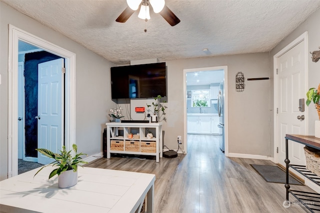 living room featuring ceiling fan, light hardwood / wood-style floors, and a textured ceiling