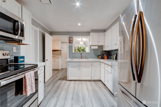 kitchen featuring sink, light hardwood / wood-style flooring, white cabinetry, stainless steel appliances, and tasteful backsplash