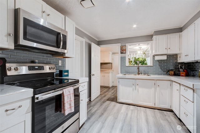 kitchen featuring backsplash, stainless steel appliances, light wood-type flooring, and white cabinets