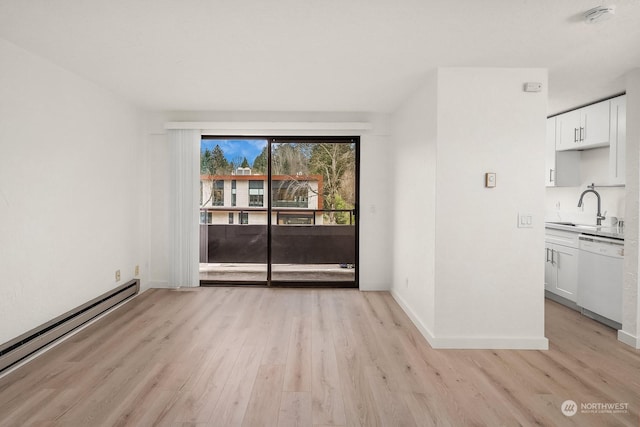 empty room with a baseboard radiator, sink, and light hardwood / wood-style floors