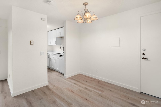 unfurnished dining area featuring sink, an inviting chandelier, and light wood-type flooring